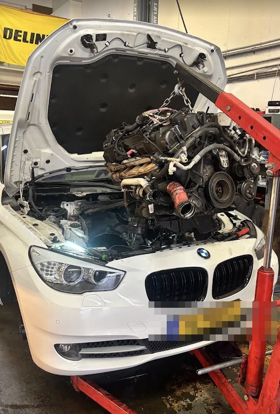 Motorwissel bij RPM Garage, complete motor gedemonteerd en uitgelicht boven een BMW